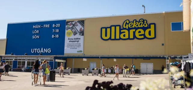 Gekås Ullared växte till 4,6 miljarder utan e-handel Röd tegelbyggnad med vita fönster bakom urban plats med trappor och moderna silverfärgade skulpturer, röd bil och parkerade cyklar.